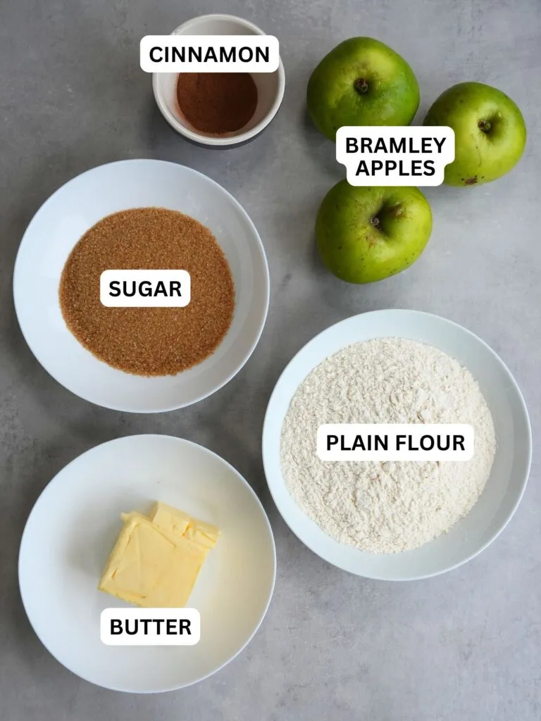 ingredients laid out and labelled for apple crumble: cinnamon, bramley apples, sugar, plain flour and butter