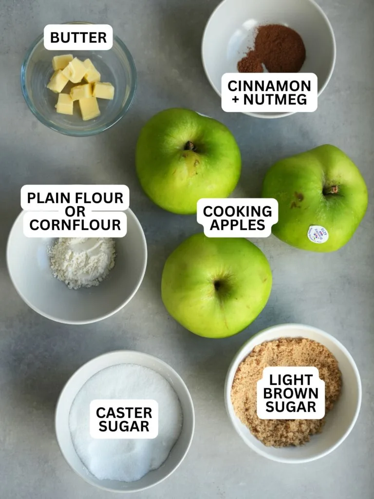 ingredients laid out and labelled for the filling of an apple pie:butter, cinnamon + nutmeg, plain flour or cornflour, cooking apples, caster sugar and light brown sugar