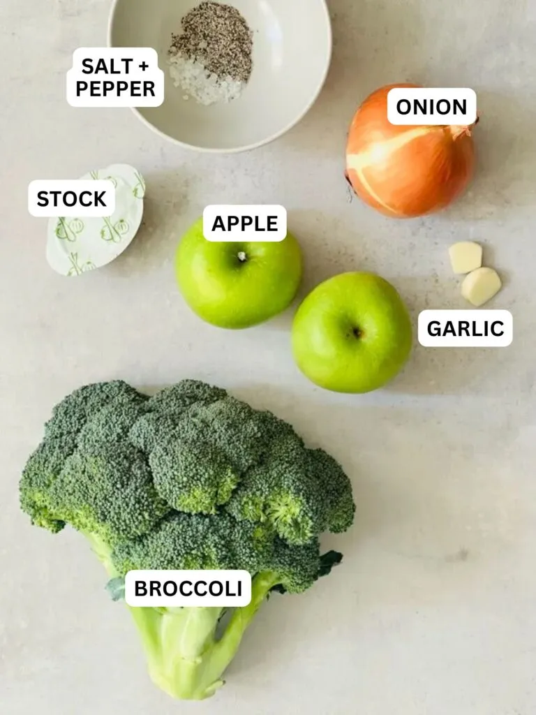 ingredients laid out and labelled for broccoli and apple soup: salt and pepper, onion, stock, apples, garlic and broccoli