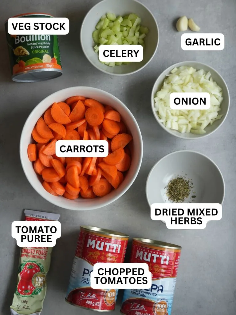 ingredients laid out and labelled for tomato and carrot soup: stock, celery, garlic, carrots, onion, dried mixed herbs, tomato puree, chopped tomatoes