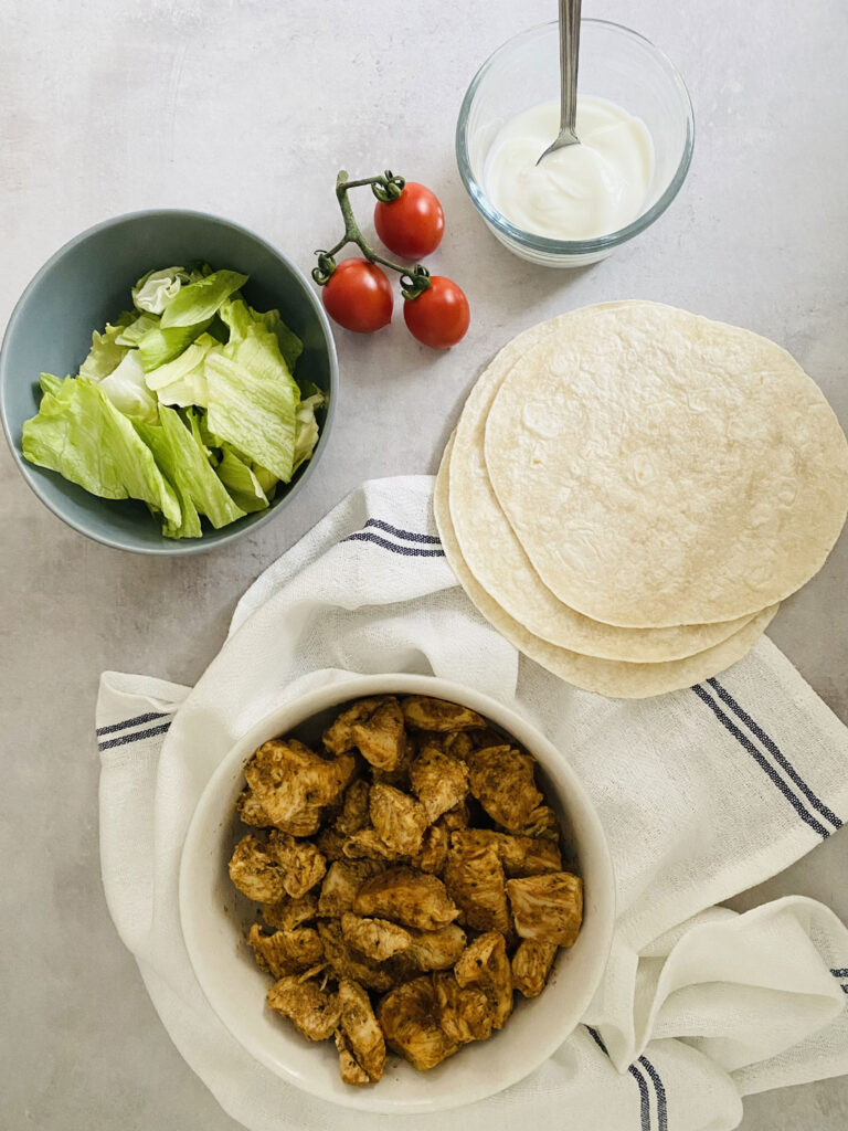 lettuce, tortilla wraps, yoghurt, cherry tomatoes and chicken tikka laid out to make a chicken tikka wrap