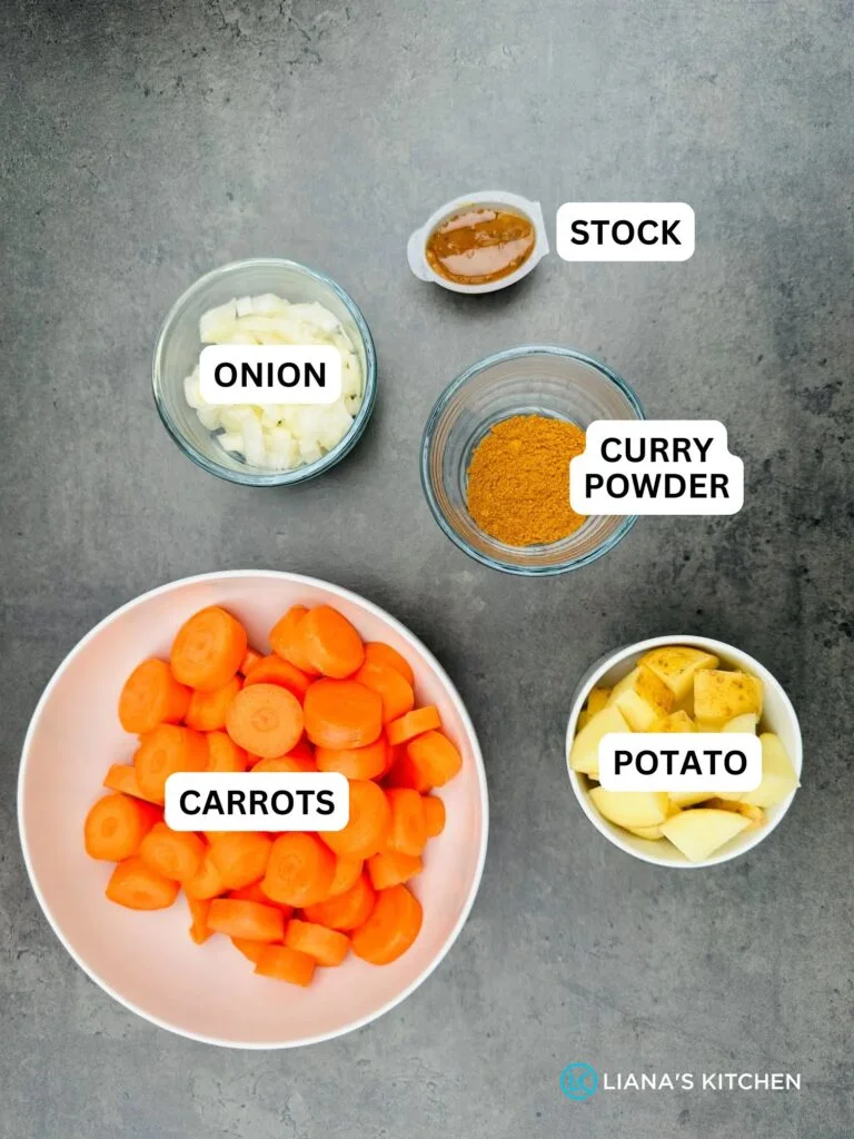 ingredients laid out for curried carrot soup: chopped carrots, potatoes, onion, stock pot and curry powder