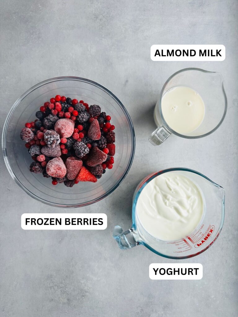 ingredients for frrozen berry smoothie: frozen berries in a glass bowl, almond milk in a jug and yoghurt in a jug