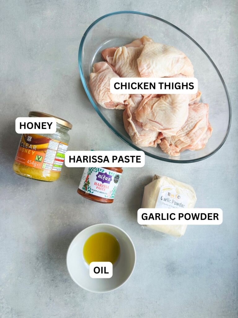 ingredients laid out and labelled for the recipe: raw bone in chicken thighs, clear honey, harissa paste, garlic powder and oil