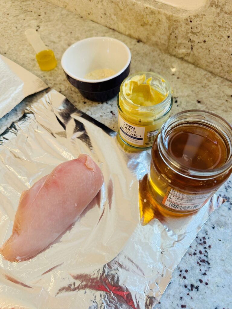 ingredients for cooking honey mustard chicken breast in an air fryer: raw chicken breast, jar of honey, Dijon mustard, garlic powder, olive oil