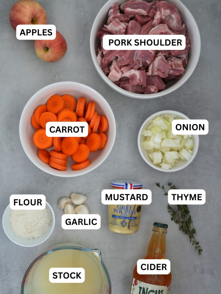 ingredients laid out and labelled for pork and cider casserole: apple, pork shoulder, carrot, onion, flour, garlic, mustard, thyme, stock and cider