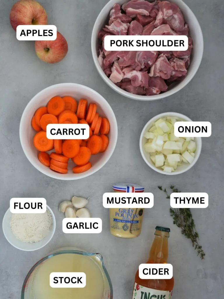 ingredients laid out and labelled for pork and cider casserole: apple, pork shoulder, carrot, onion, flour, garlic, mustard, thyme, stock and cider