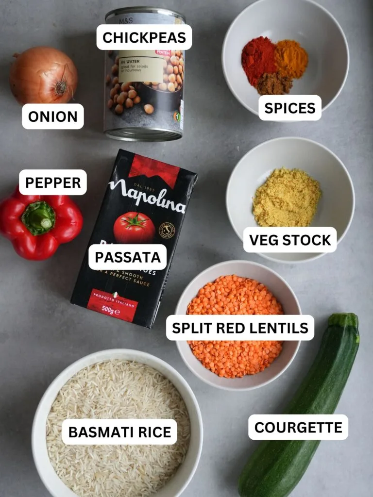 image with ingredients laid out and labelled for chickpea, lentil and vegetable rice for the rice cooker: onion, chickpeas, spices, pepper, passata, veg stock, split red lentils, basmati rice, courgette