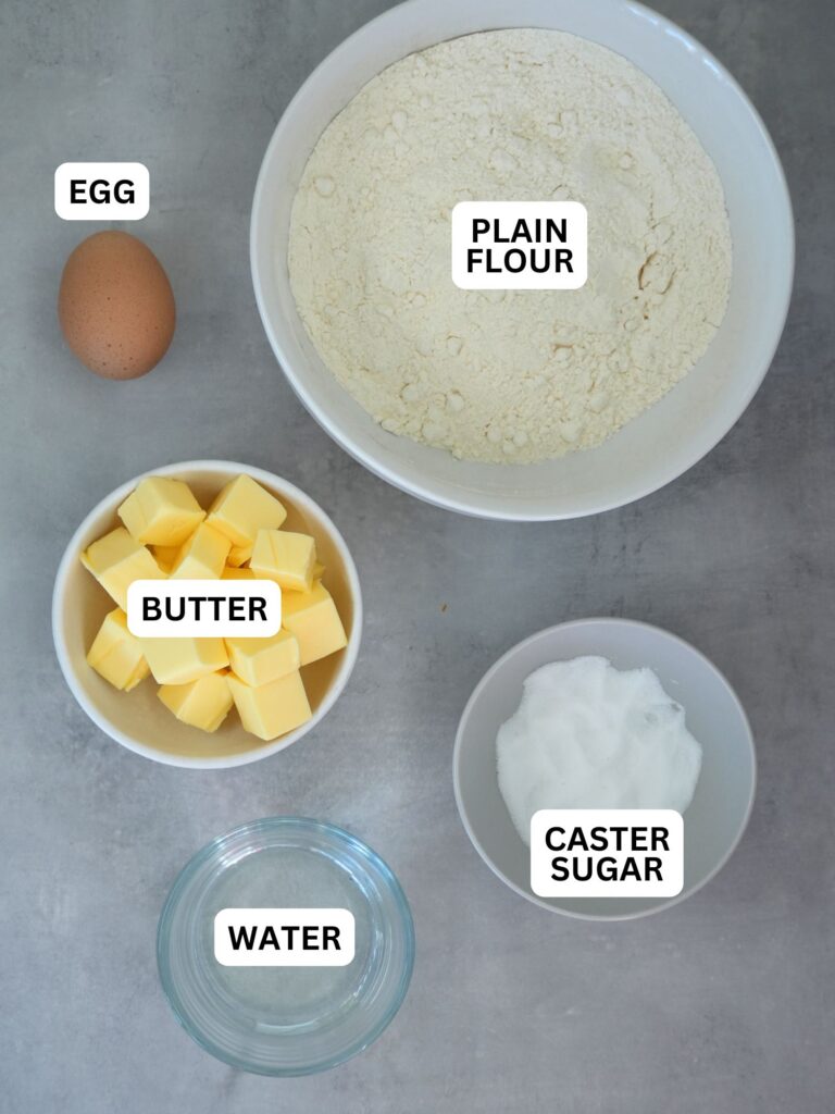 ingredients laid out and labelled for shortcrust pastry; egg, plain flour, butter, caster sugar and water