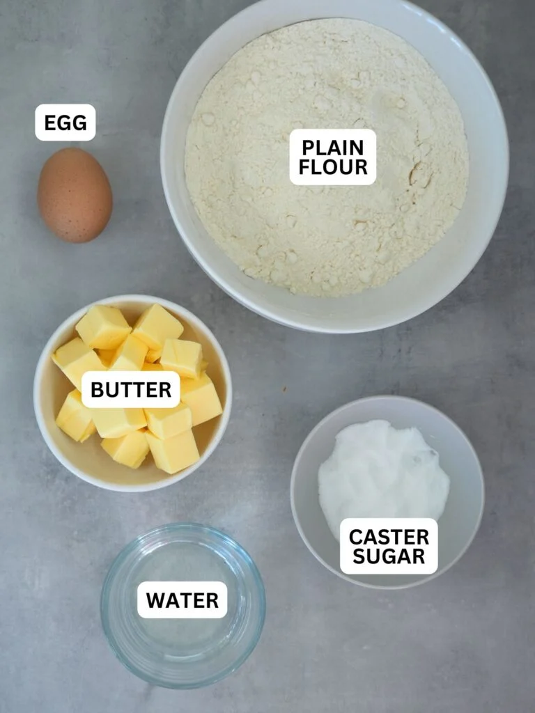ingredients laid out and labelled for shortcrust pastry; egg, plain flour, butter, caster sugar and water