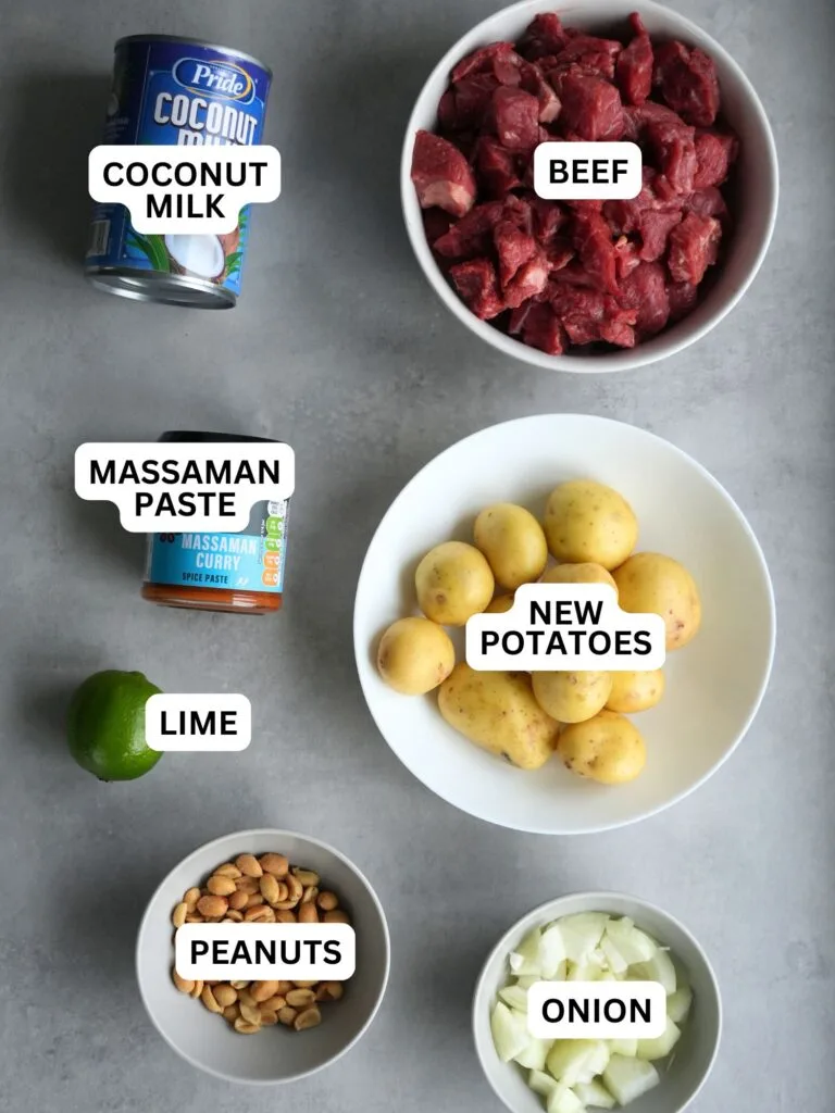 ingredients laid out and labelled for slow cooker massaman inspired beef curry: coconut milk, beef, massaman paste, new potatoes, lime, peanuts and onion