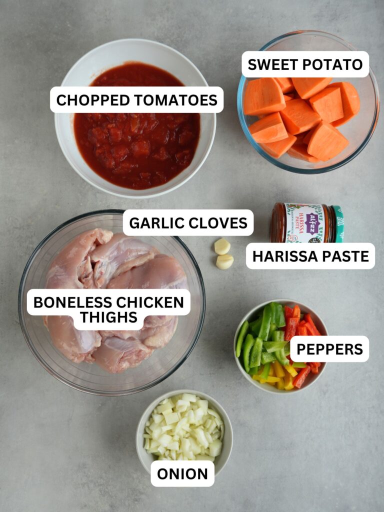 ingredients laid out for slow cooker chicken and sweet potato, labelled: tomatoes, sweet potatoes, chicken, garlic cloves, harissa paste, peppers, onion