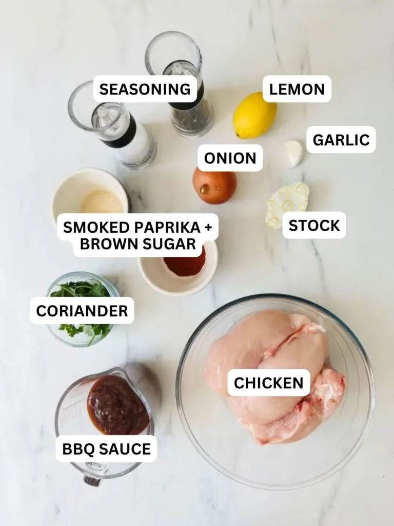 ingredients laid out and labelled for slow cooker pulled chicken: seasoning, lemon, onion, garlic, stock, smoked paprika and brown sugar, coriander, BBQ sauce and chicken