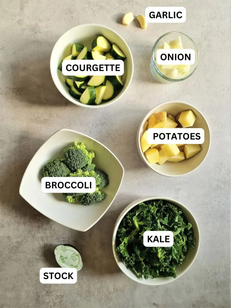 ingredients laid out and labelled for green soup in a soup maker: courgette, onion, potatoes, broccoli, stock and kale