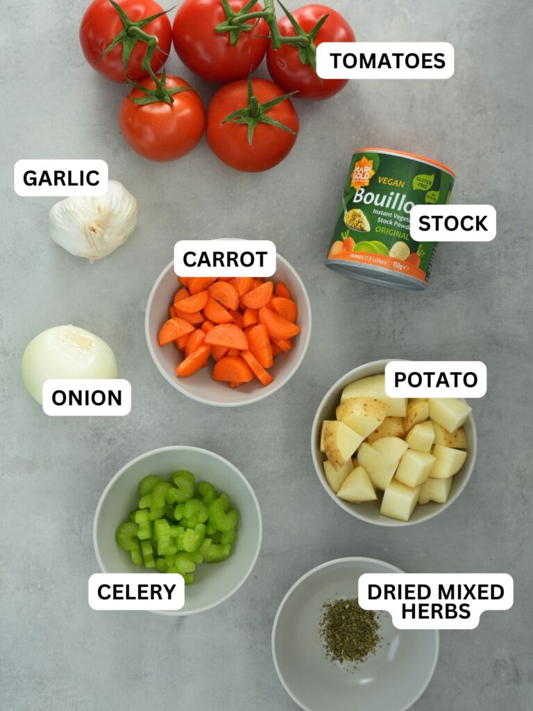 ingredients laid out and labelled for roasted tomato and garlic soup: tomatoes, garlic, carrot, stock, onion, potato, celery and dried mixed herbs