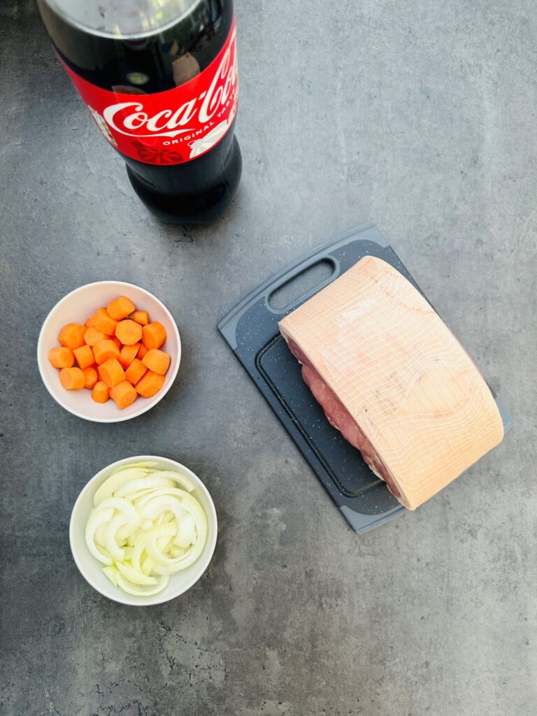 ingredients for slow cooker gammon in coke: gammon joint, chopped carrots, chopped onion and coke bottle