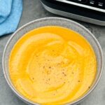 Jamaican Jerk sweet potato soup in a bowl next to a soup maker