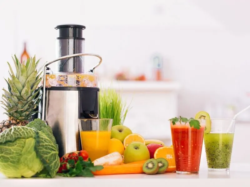 juicer with fresh fruit and vegetables and juice in glasses
