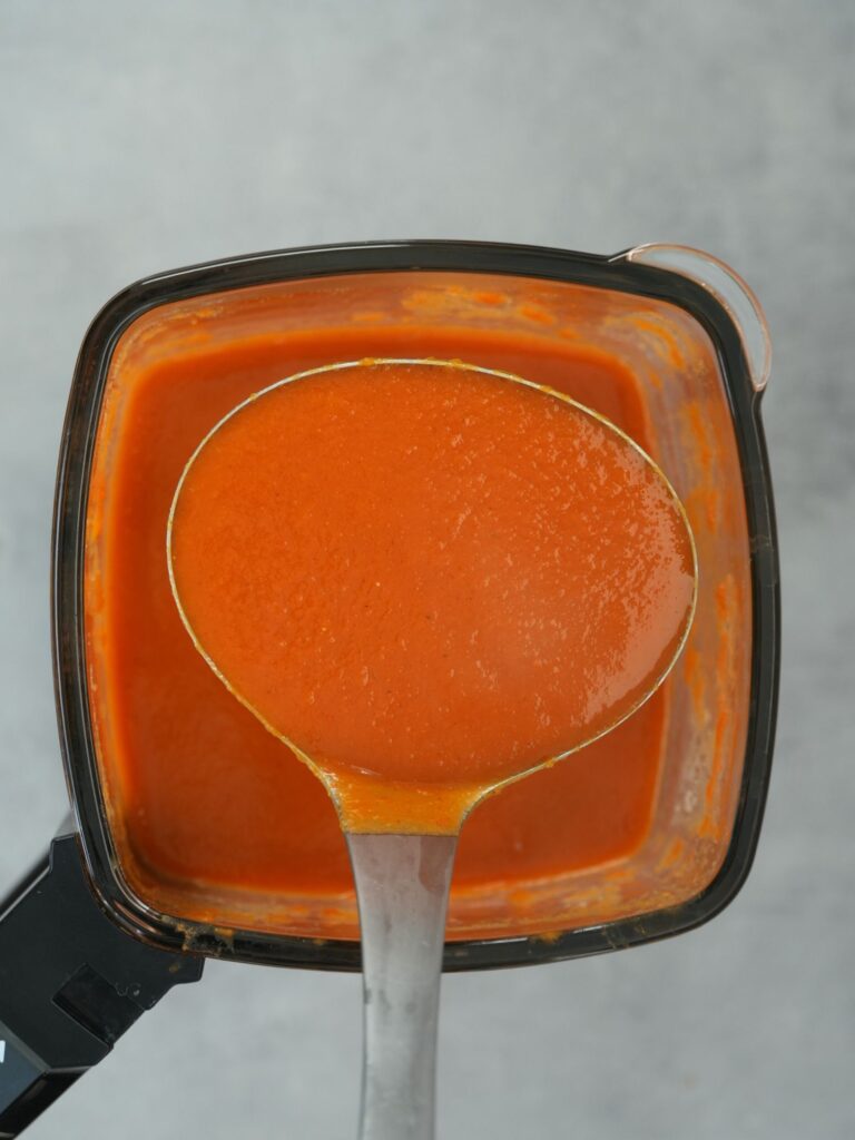 ladle of tomato and butter bean soup above a Ninja soup maker jug