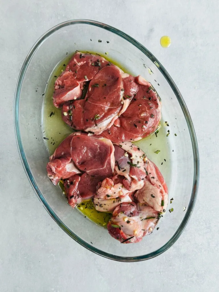 raw lamb steaks in a bowl with olive oil fresh crushed garlic and fresh chopped rosemary