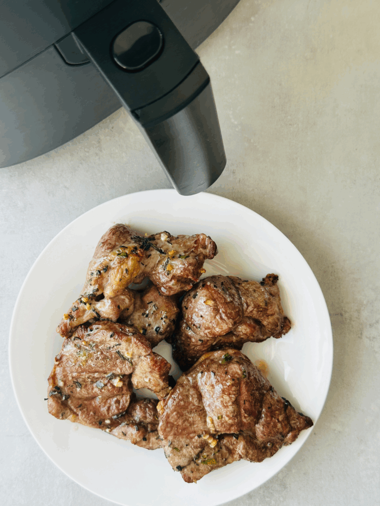 cooked lamb steaks on a white plate next to air fryer