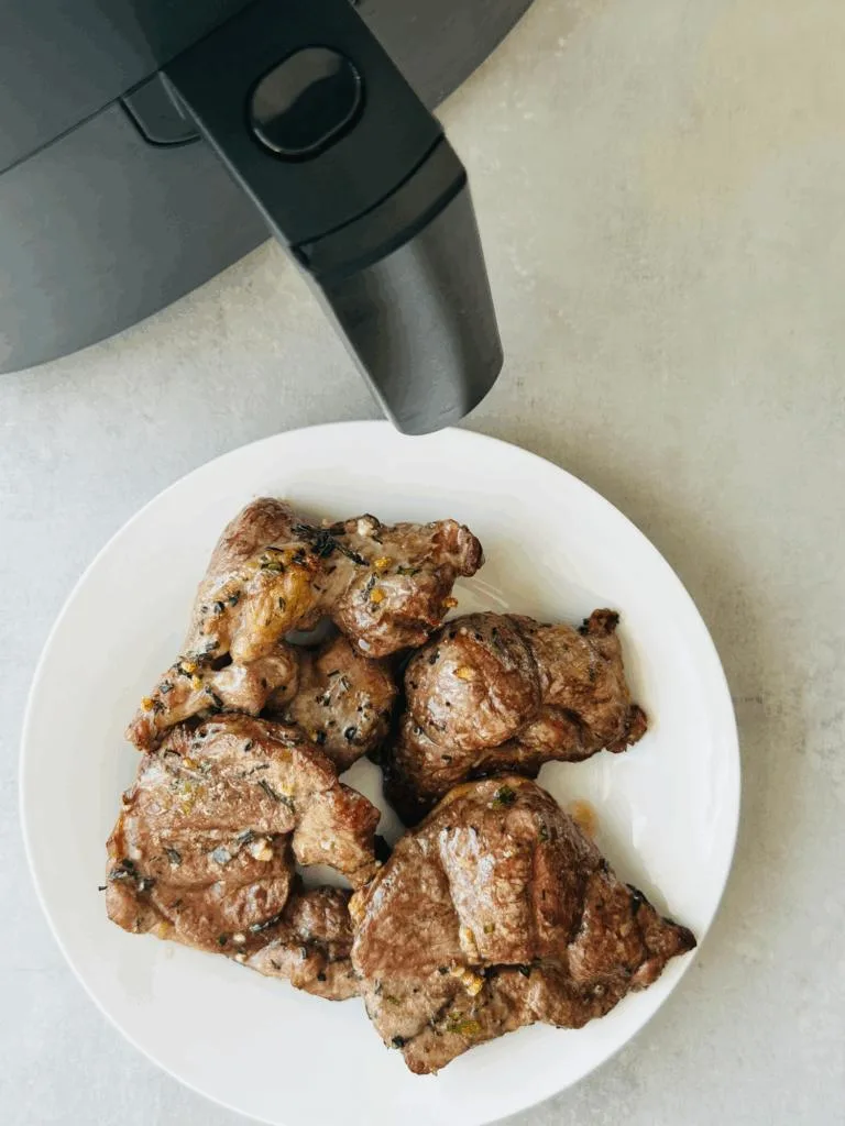 cooked lamb steaks on a white plate next to air fryer