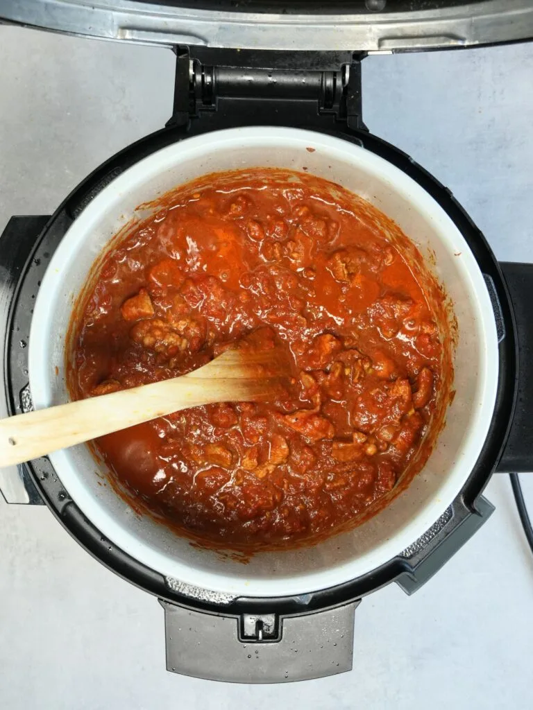 cooked lamb curry simmering down in the Ninja pot with a wood spatula spoon in it