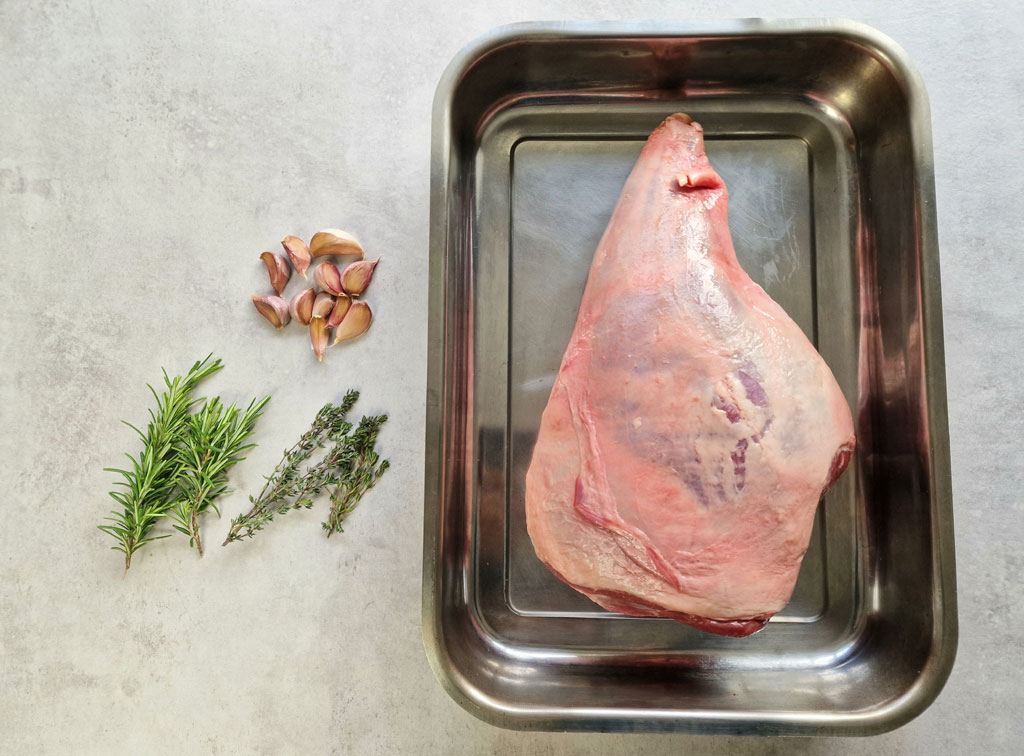 leg of lamb in roasting tin with rosemary, thyme and garlic cloves