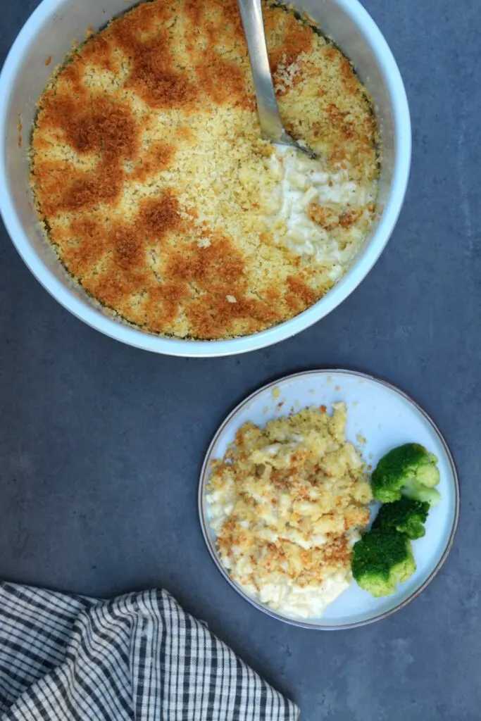 baked macaroni cheese in a Ninja Foodi bowl with a serving on a plate with a broccoli.