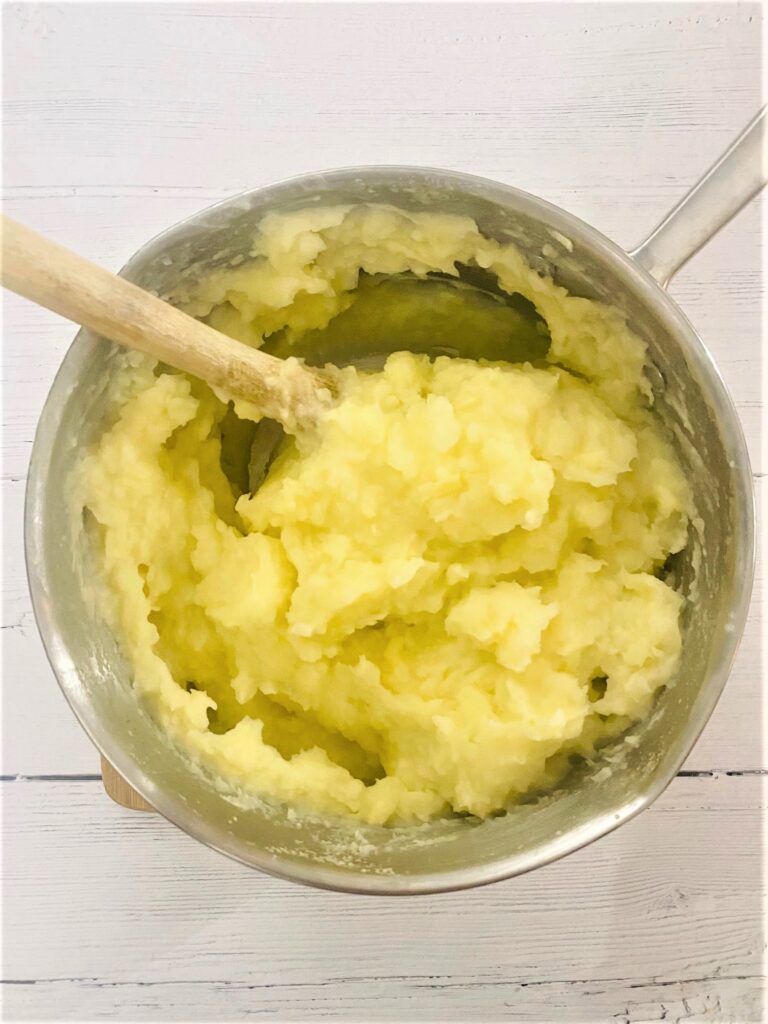 mashed potato in saucepan with wooden spoon ready to put on cottage pie