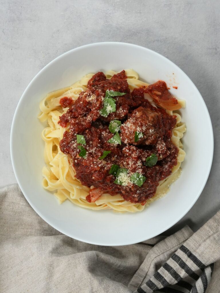 slow cooked meatballs on top of pasta with fresh basil leaves on top