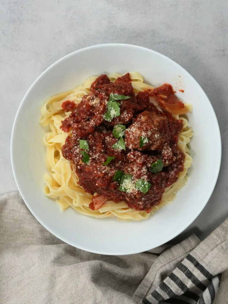 slow cooked meatballs on top of pasta with fresh basil leaves on top