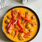 meatballs cooked in air fryer place in bowl with Thai red curry sauce poured over the top