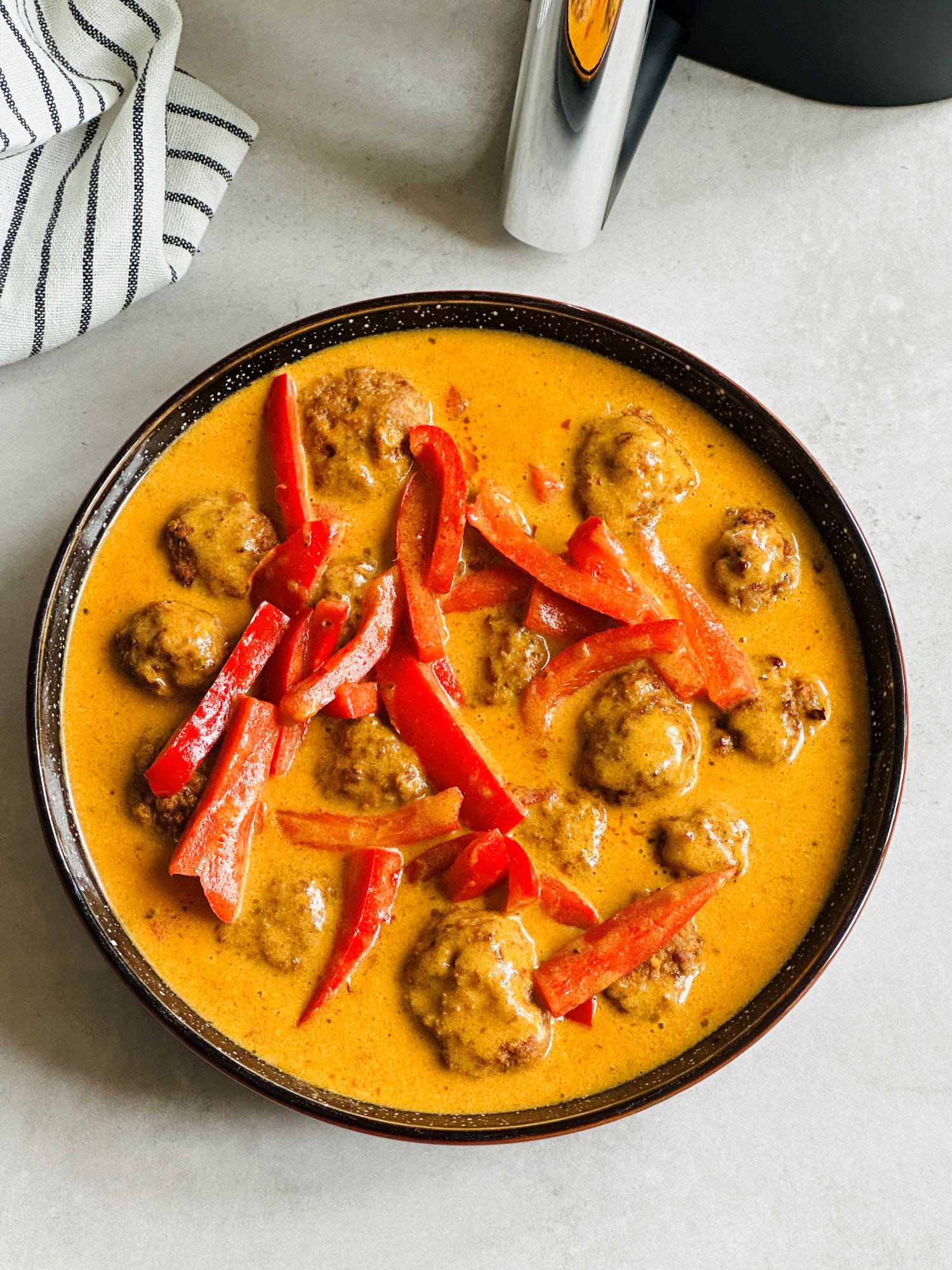meatballs cooked in air fryer place in bowl with Thai red curry sauce poured over the top