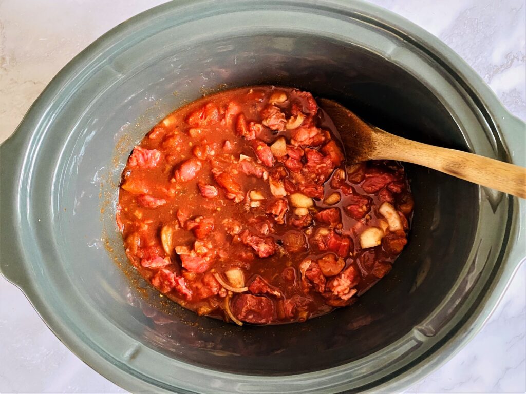 slow cooker with Mexican beef stew ingredients and wooden spoon