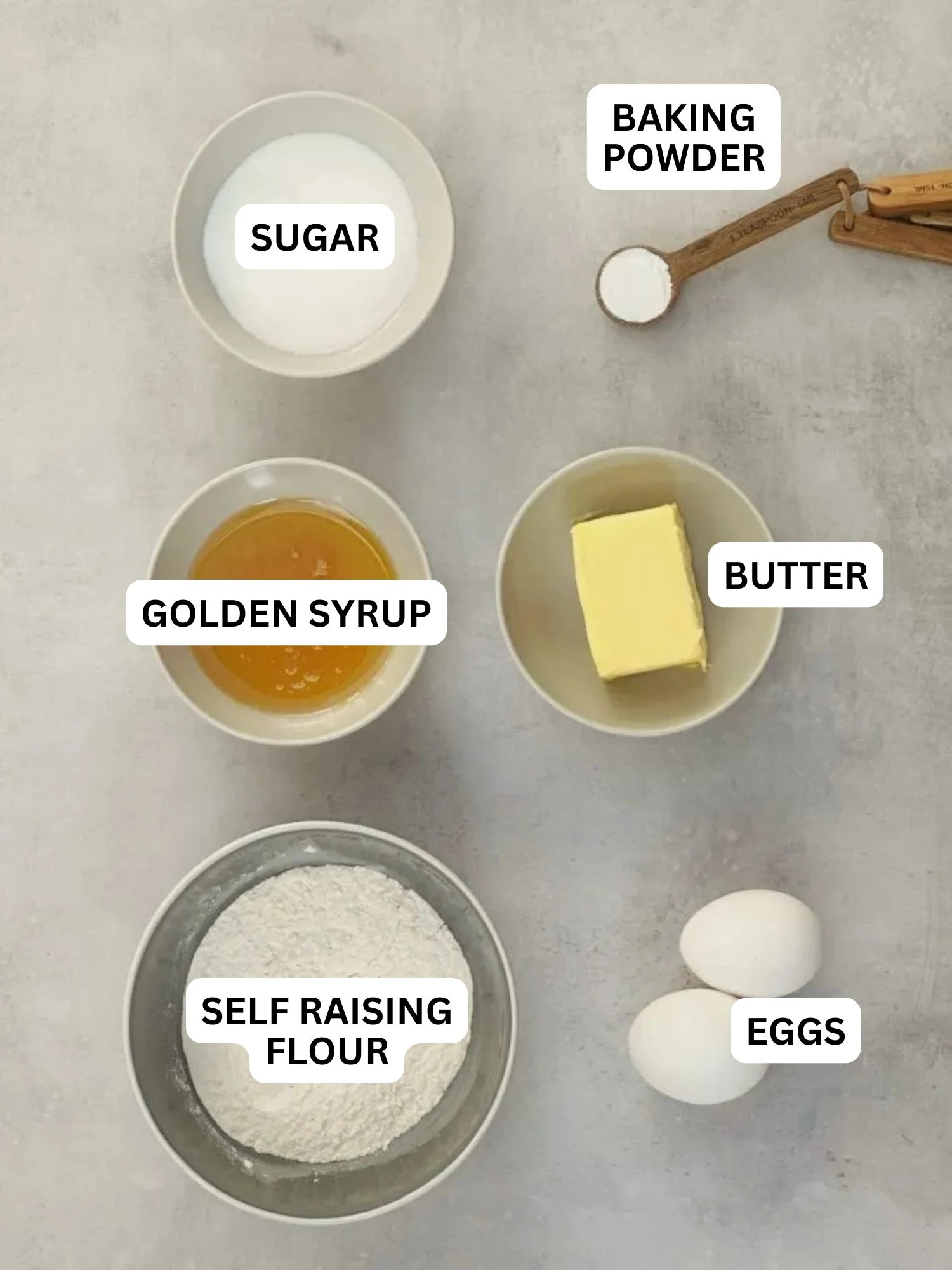 ingredients laid out and labelled for microwave treacle sponge pudding: sugar, baking powder, golden syrup, butter, self raising flour, eggs
