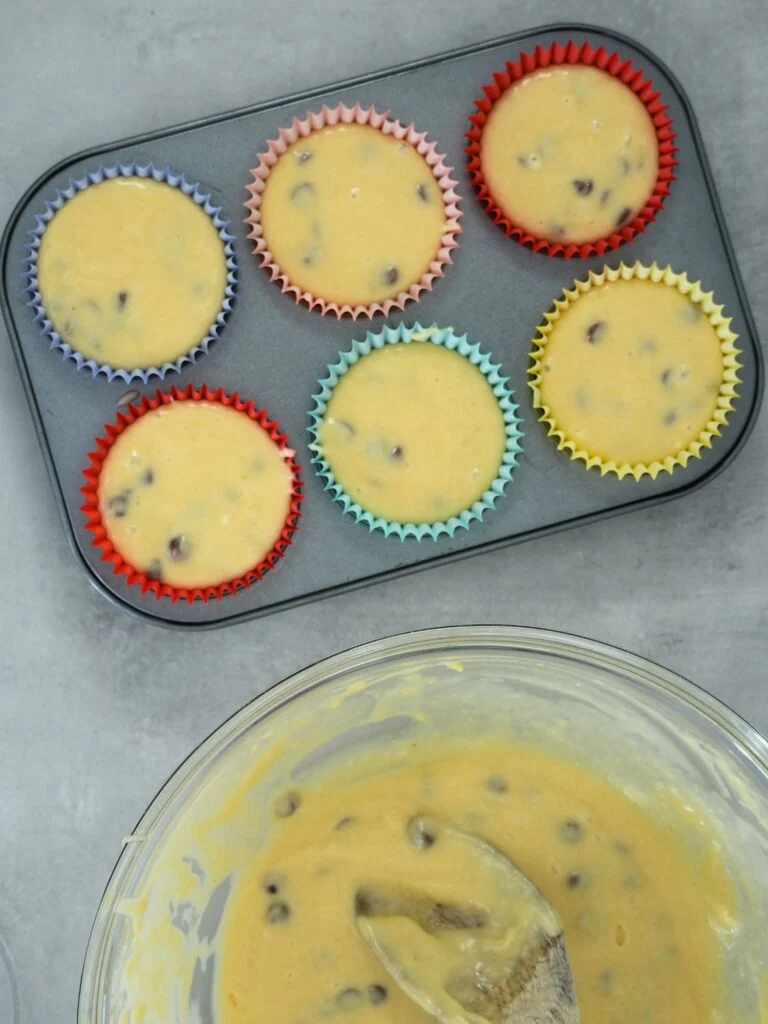 muffin batter in baking tin next to a mixing bowl with batter mix in it