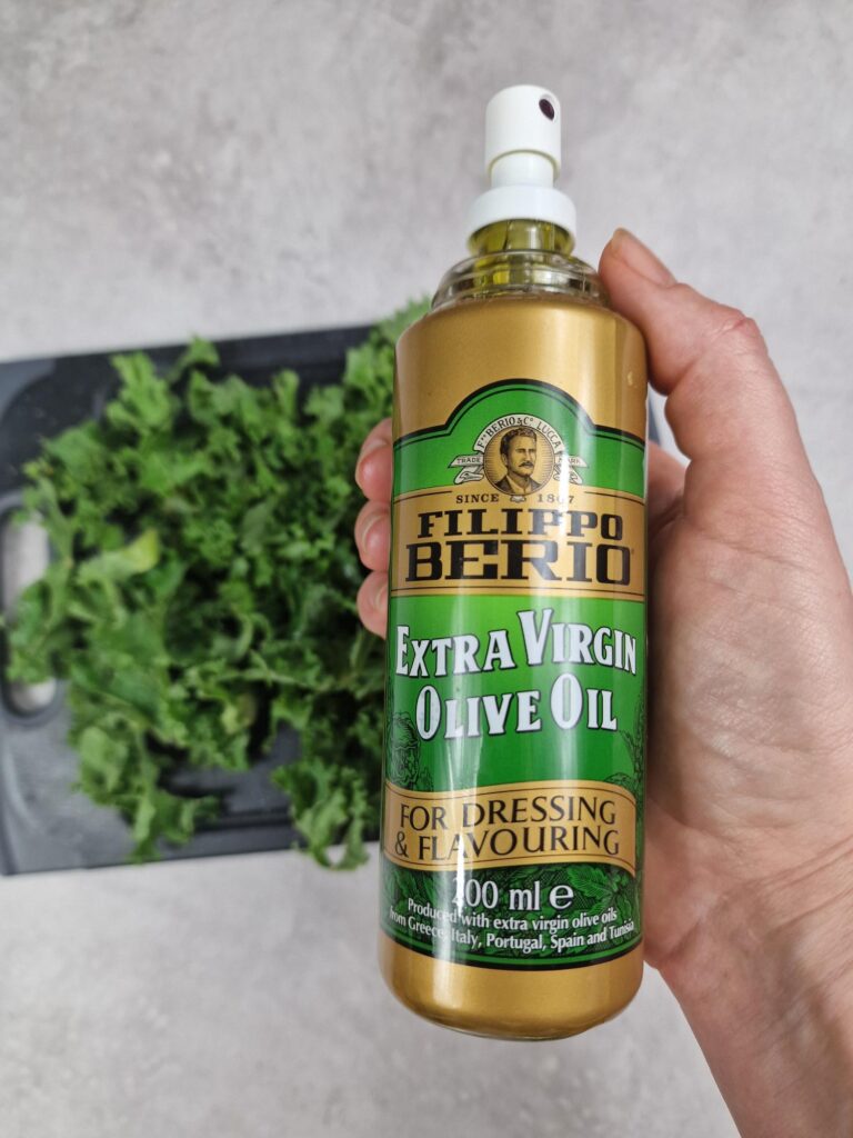 olive oil spray bottle above raw shredded kale on chopping board