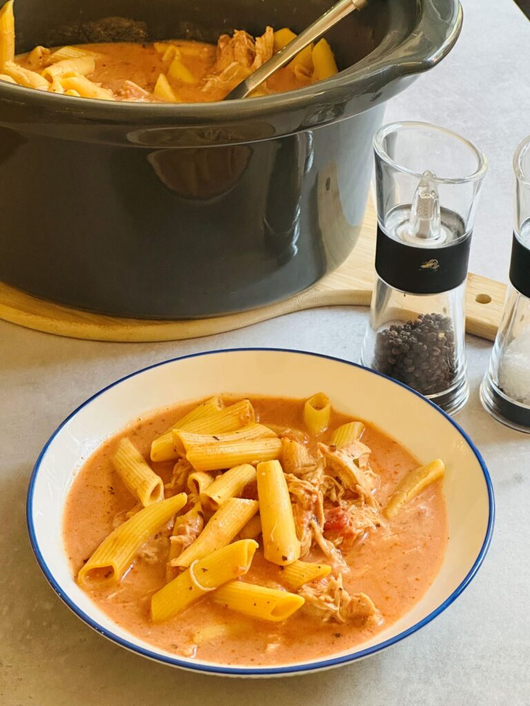 bowl of chicken and pasta next to a slow cooker pot and salt and pepper shakers