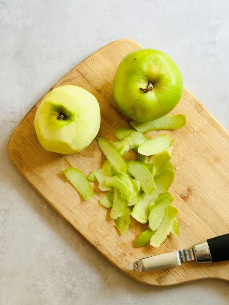 two Brmaley apples being peeled and prepared for chopping