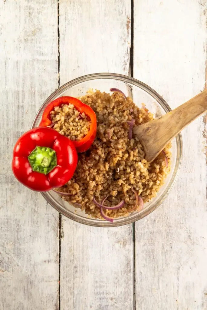 Cooked rice and onions in a bowl with a stuffed pepper resting on top, ready to be transferred to a slow cooker.  