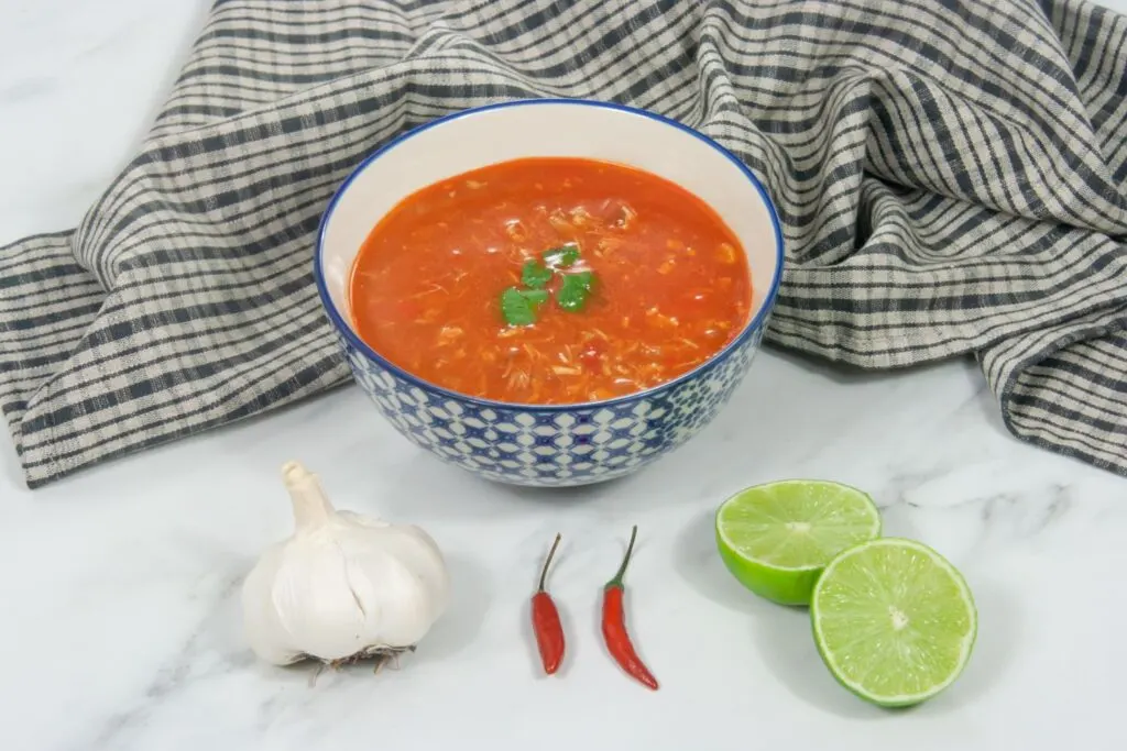 piri piri chicken soup in a bowl next to garlic, chillies and lime