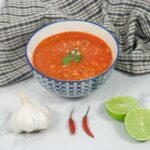 piri piri chicken soup in a bowl next to garlic, chillies and lime
