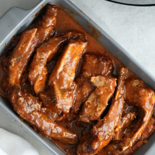 slow cooked bbq ribs in a sauce served in an oven dish next to a slow cooker