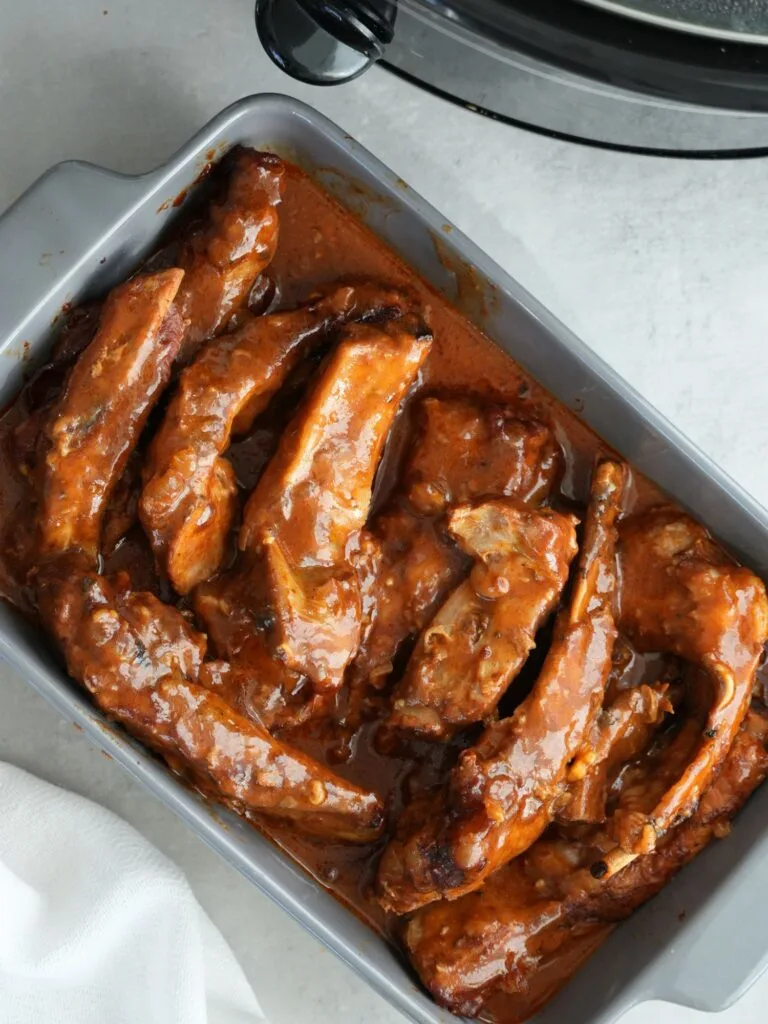 pork ribs in a bbq sauce in a serving dish next to a slow cooker