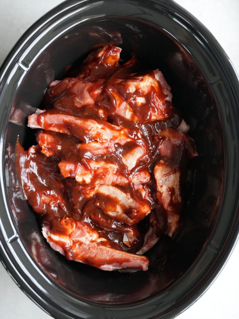 raw pork ribs in slow cooker with bbq sauce poured on top
