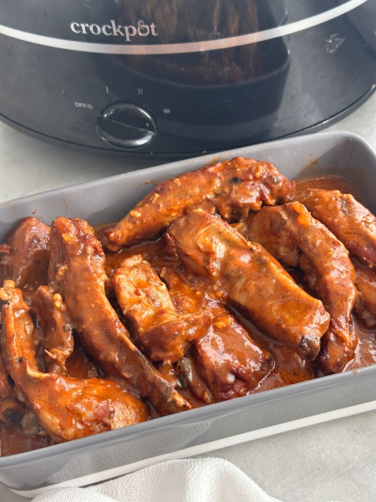 slow cooked pork ribs served in a dish covered with bbq sauce in front of a crockpot slow cooker 