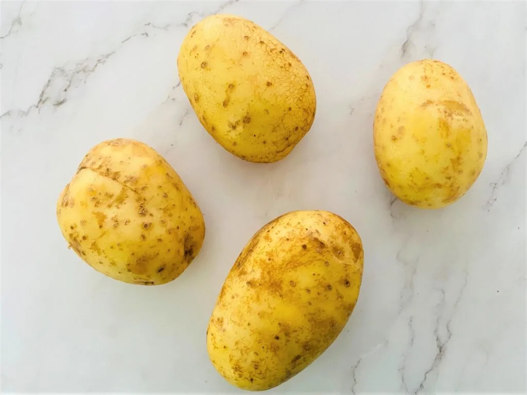 4 Maris Piper potatoes with skin on, cleaned ready to be cut into potato wedges for cooking in an air fryer