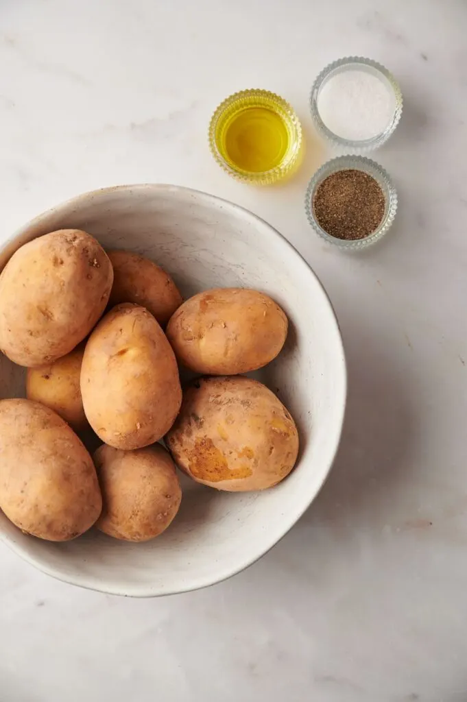 whole raw potatoes in a bowl next to oil and seasonings