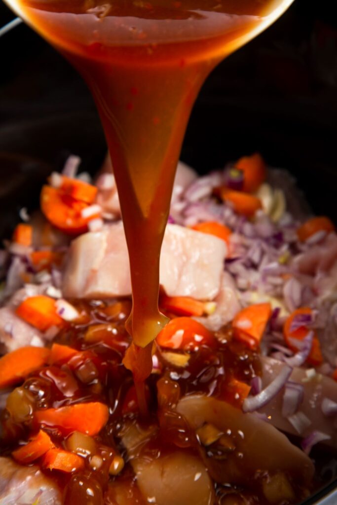 pouring sweet and sour sauce on chicken in slow cooker